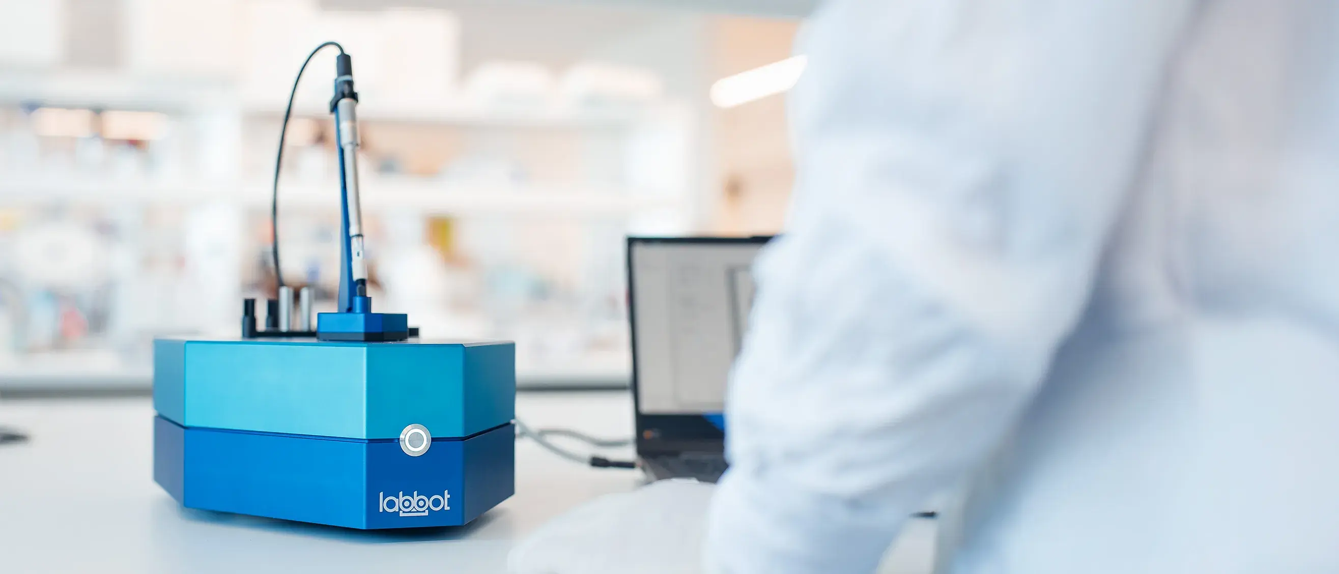 The Labbot instrument on a lab bench, with a scientist working at a laptop beside it